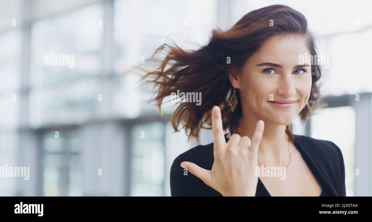 I make the business world rock. Cropped shot of a young businesswoman showing a shaka hand sign while walking through a modern office. Stock Photo