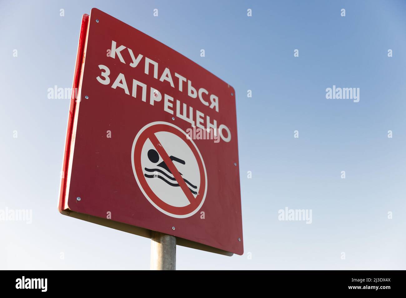 Swimming is prohibited, red sign with Russian text is under clear blue sky Stock Photo