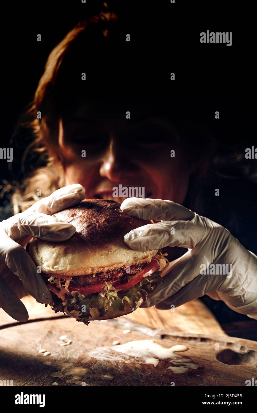 A girl holds a hamburger in her hands in gloves Stock Photo