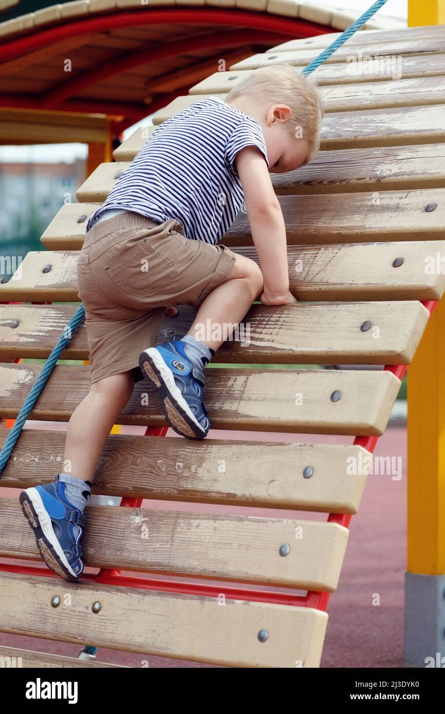Child trying to climb up on a wall in outdoor playground. Strong boy never give up Stock Photo