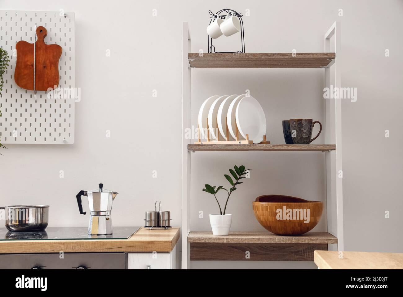 Modern shelving unit with tableware and coffee maker on stove near white wall in kitchen Stock