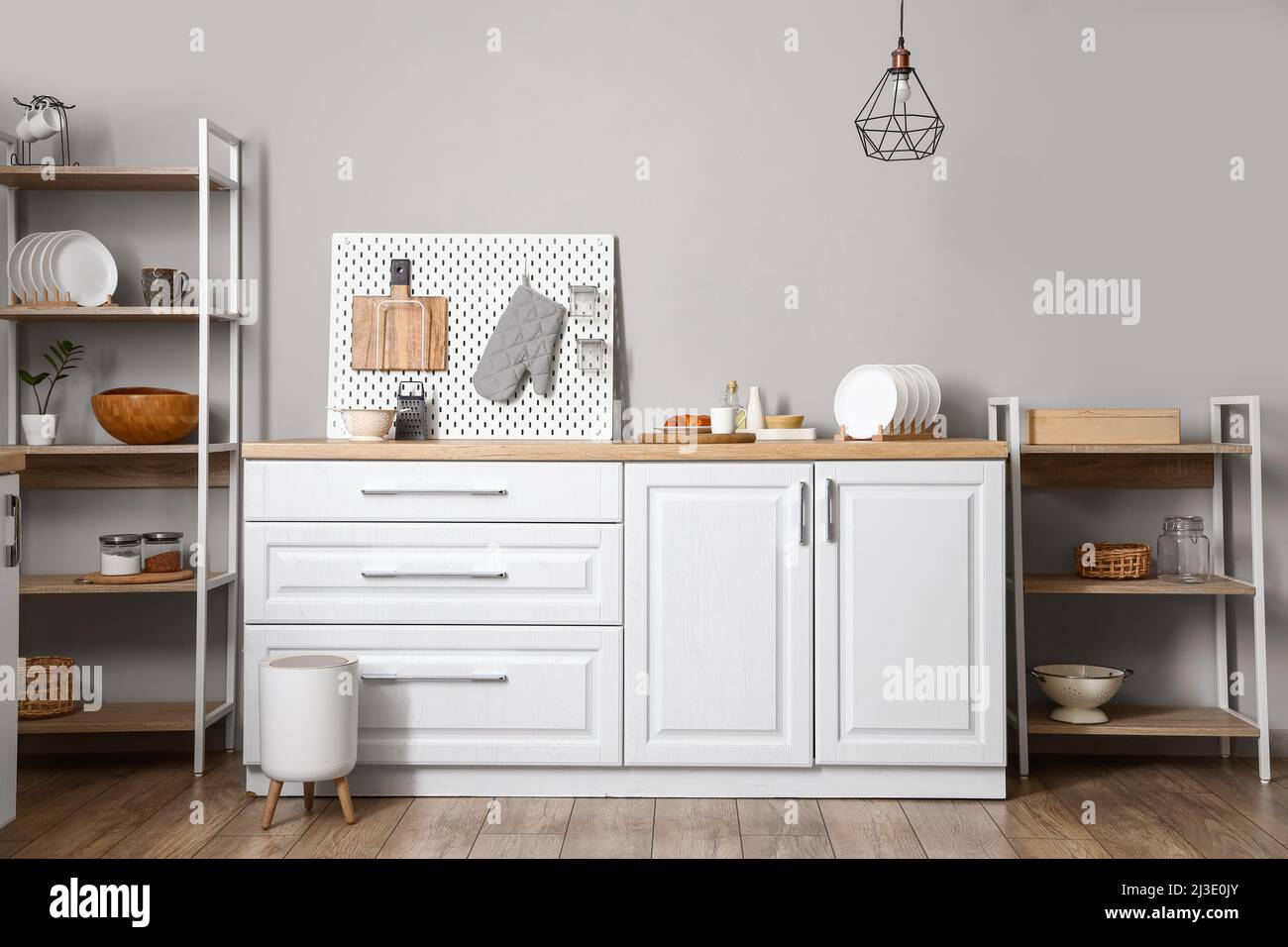 Modern shelving unit with dishware, pegboard and counter near light ...