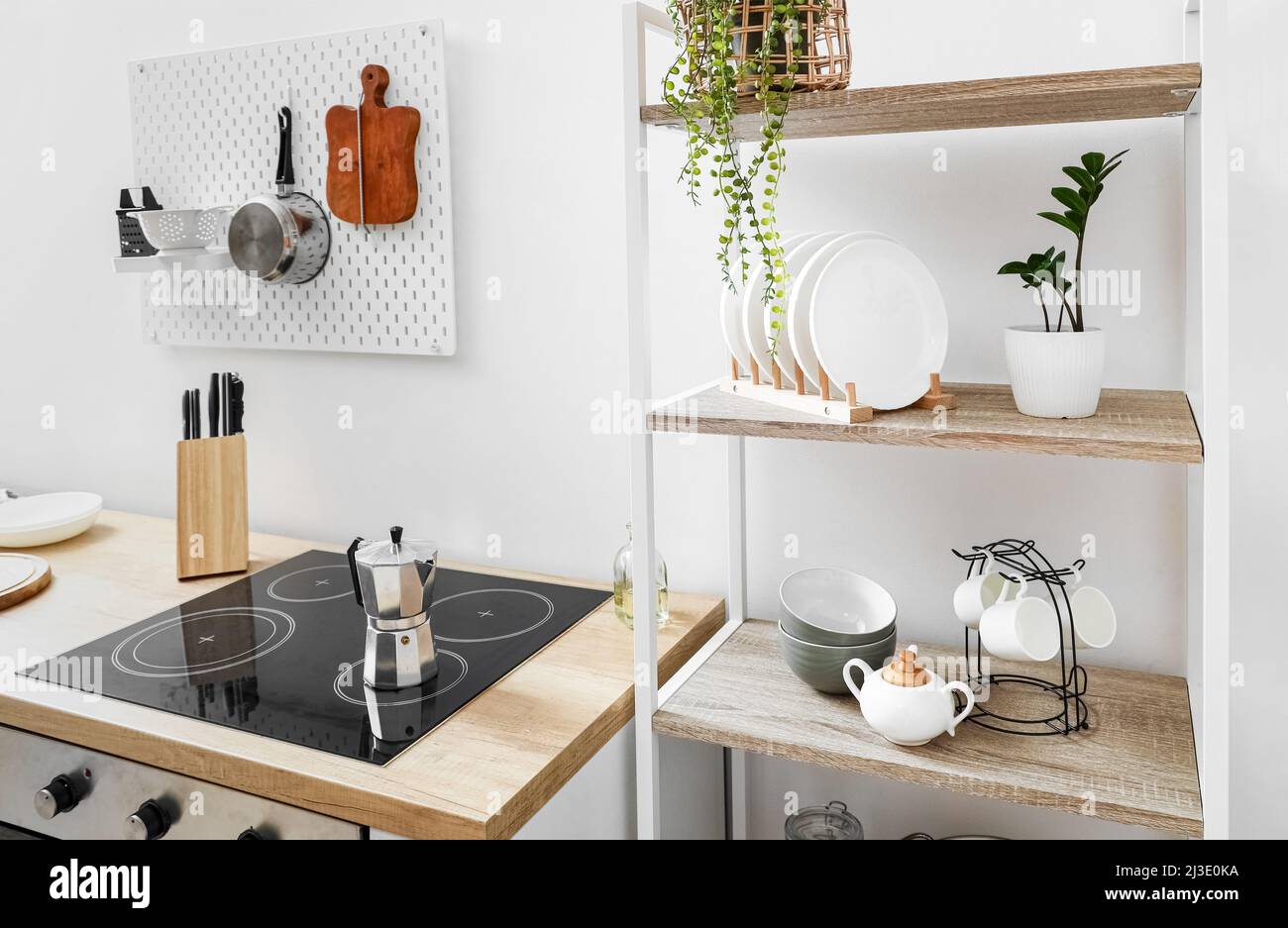 Modern shelving unit with tableware, pegboard and coffee maker on electric stove near white wall
