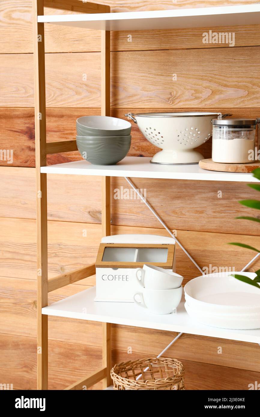 Modern shelving unit with dishware near wooden wall in kitchen Stock