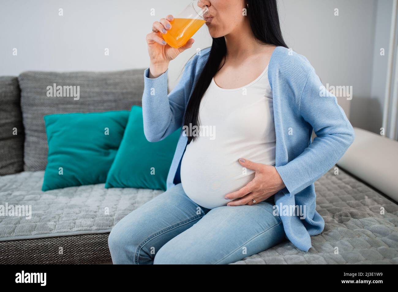 A pregnant woman drinks orange juice in the living room and holds her ...
