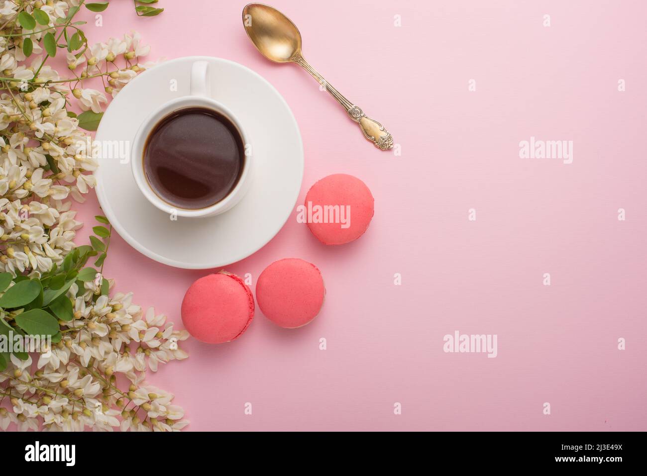 Spring floral background with coffee and macaroons, textures and wallpaper. Flat white flowers on a light pink background, top view, copy space. Festi Stock Photo