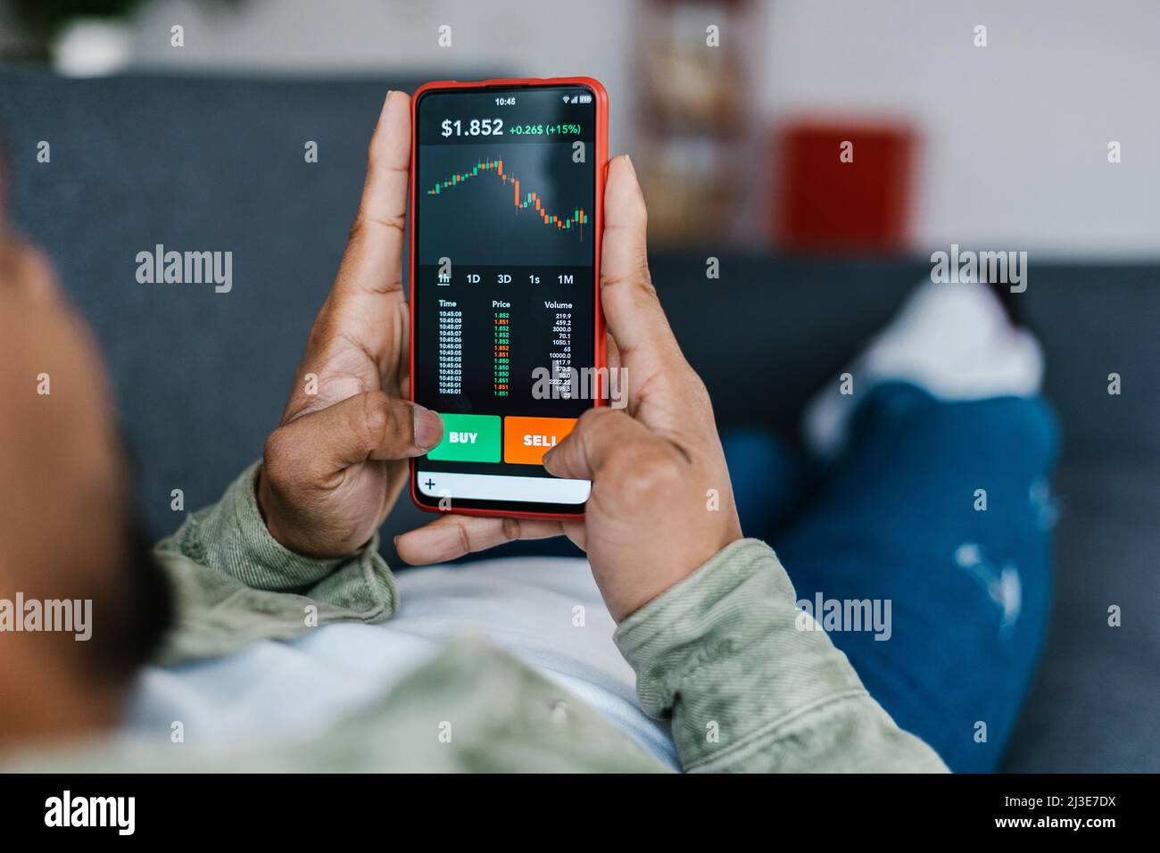 Multiracial man lying on sofa and holding phone with stock market app  Stock Photo