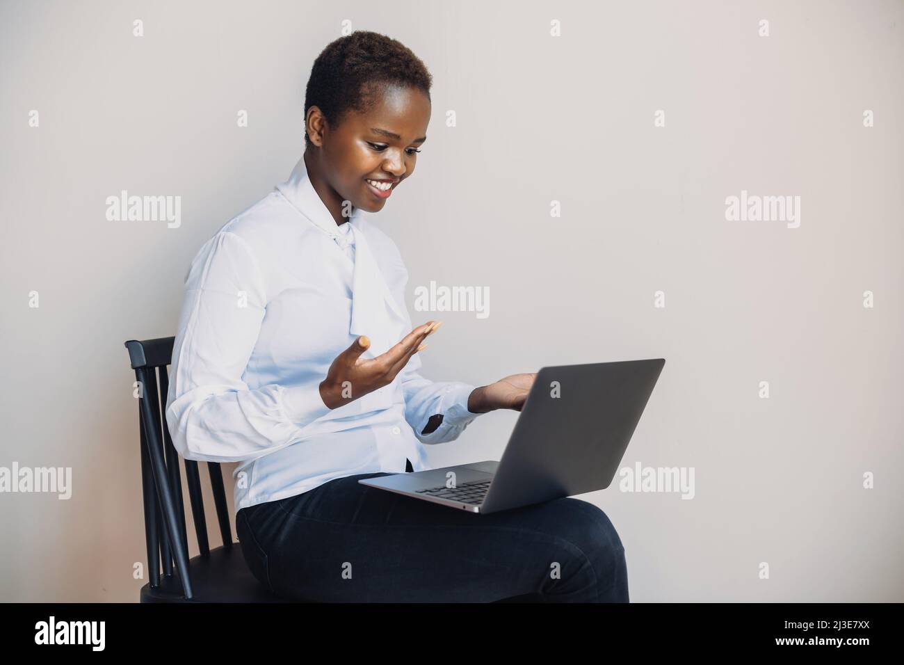 African woman sitting on a chair on white wall and working on a laptop ...