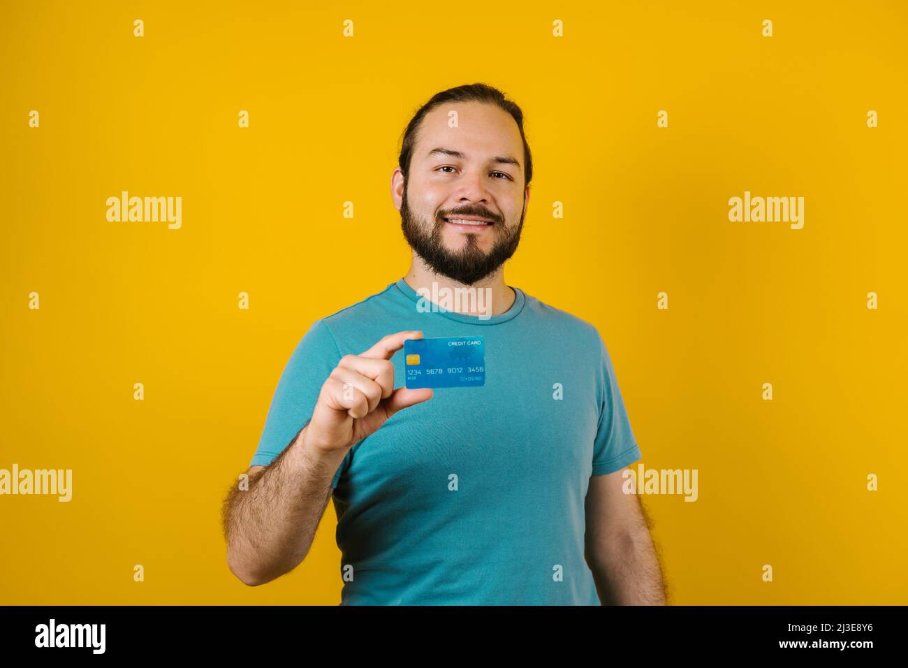 young latin man holding a credit card for shopping on yellow background in Mexico Latin America Stock Photo