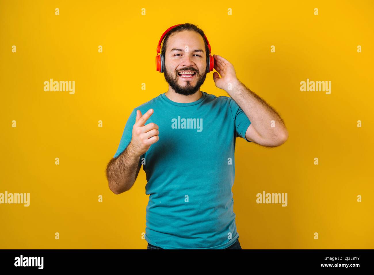 portrait of hispanic young man with headphones, dancing and listening music on yellow background in Mexico Latin America Stock Photo