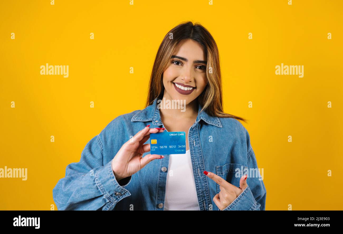 young latin woman holding a credit card for shopping on yellow background in Mexico Latin America Stock Photo