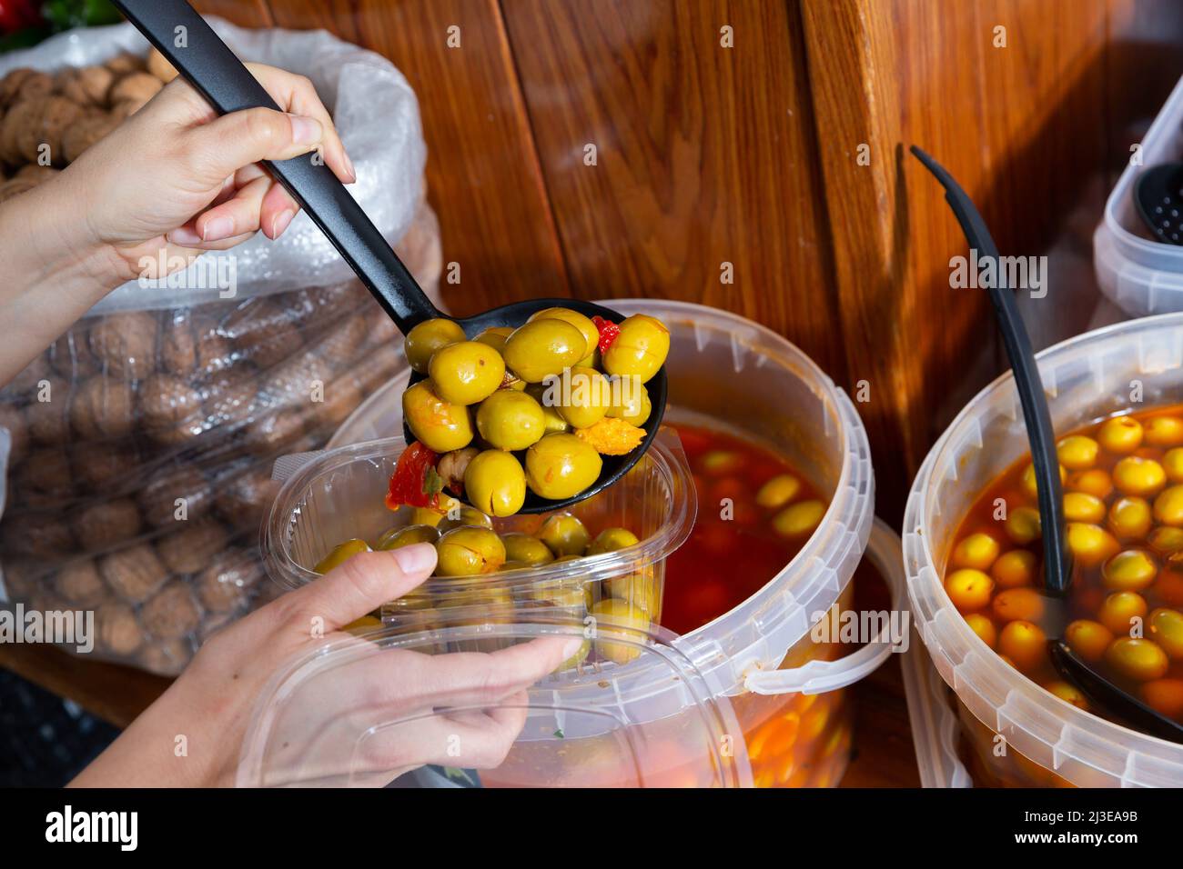 Hands of buyer pouring pickled olives by weight into plastic container
