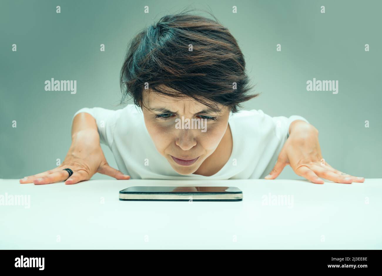 woman looks suspiciously at her cell phone up close, doesn't trust technology because nothing ever works and is afraid of viruses and threats from the Stock Photo