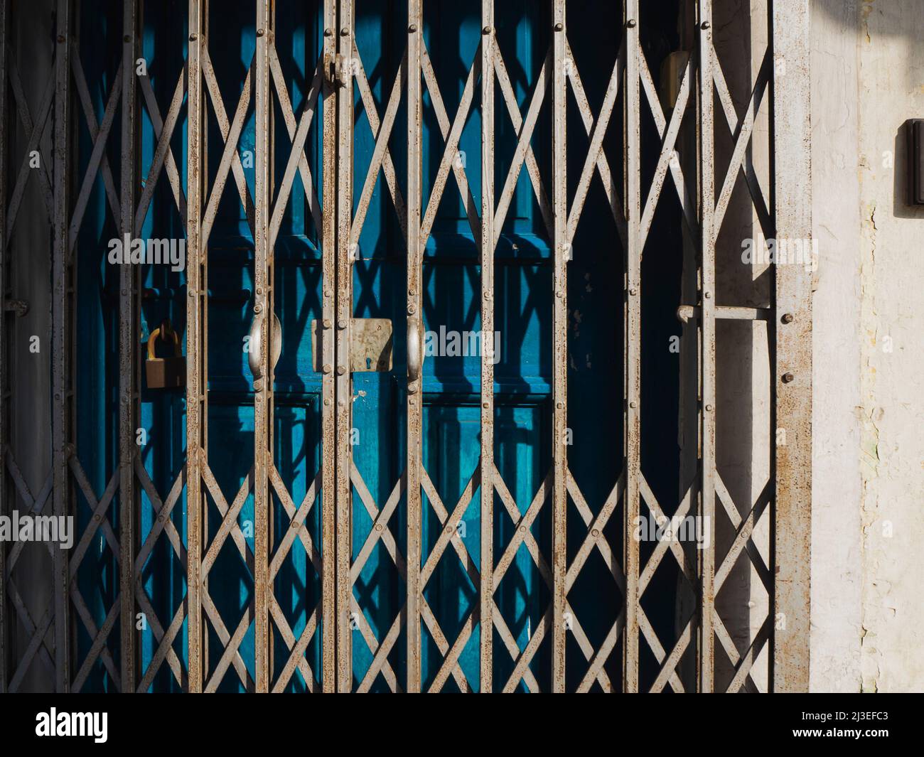 An old, rusty metal grill gate in front of blue wooden doors Stock Photo