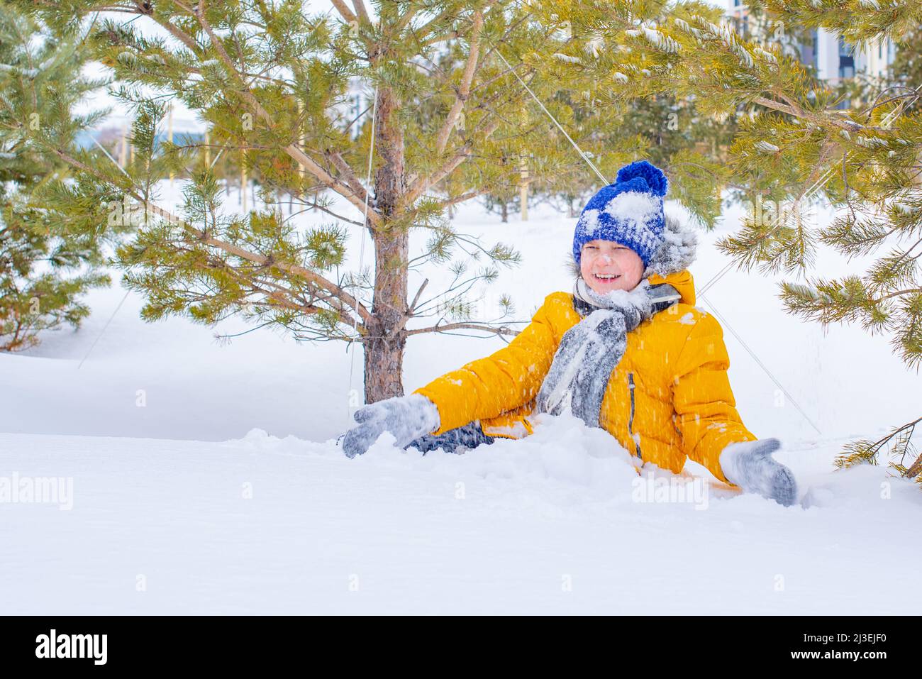 in a yellow jacket and a blue hat boy playing in the snow Stock Photo