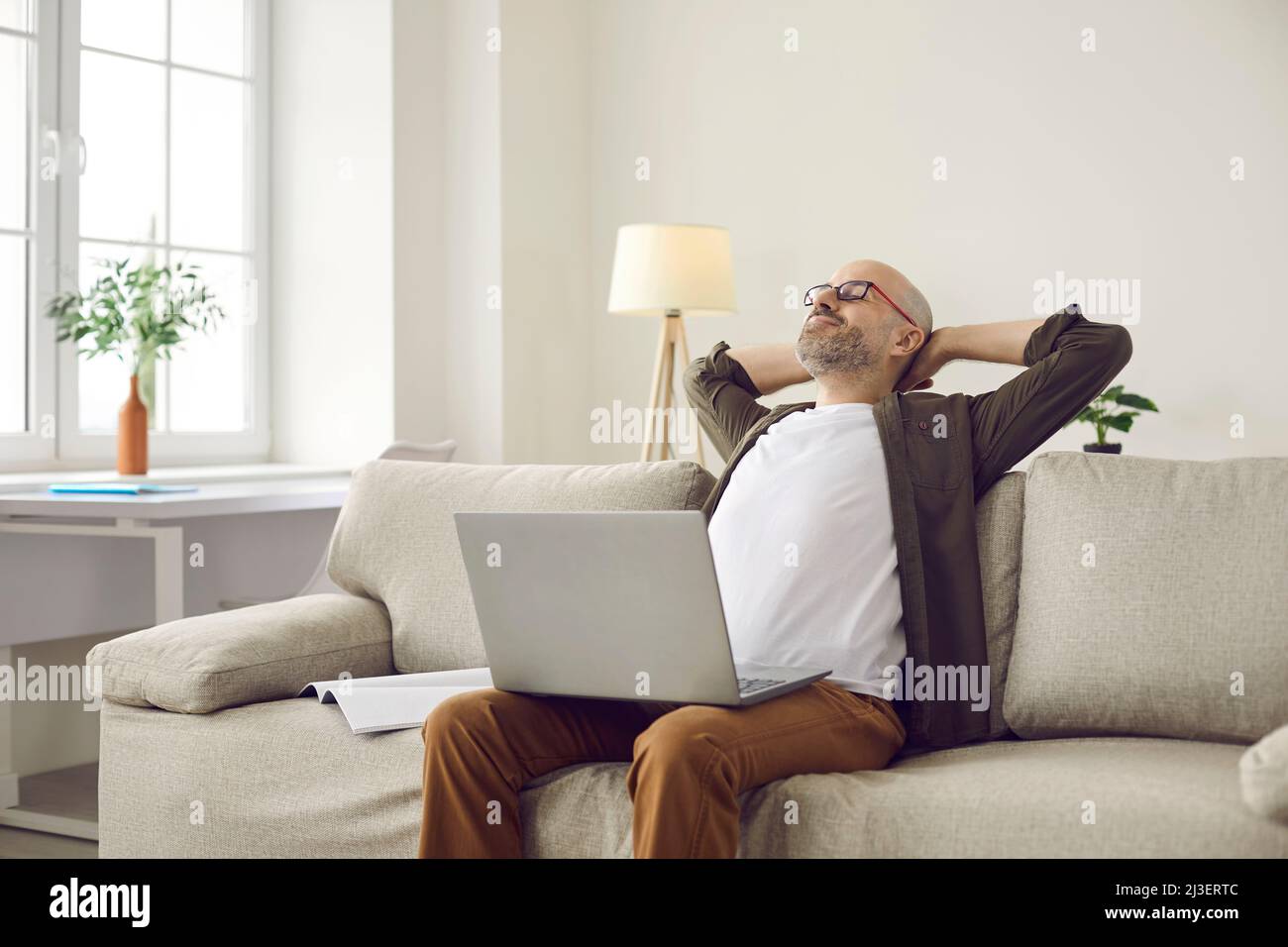 Smiling man puts his hands behind his head taking break after working with laptop. Stock Photo