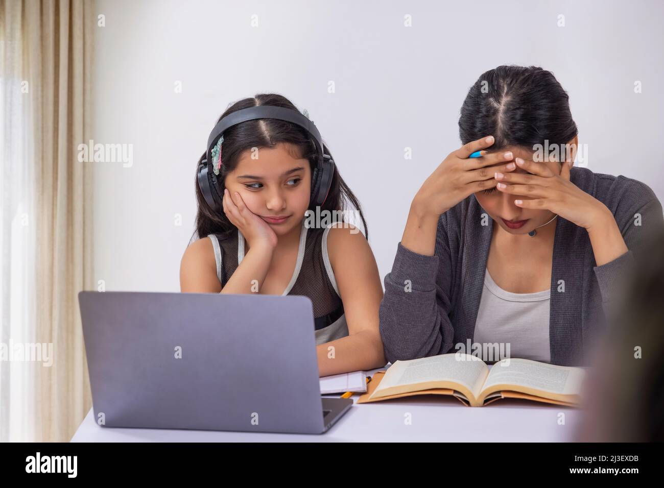 Girl studying online using laptop and mother reading book with hands on head Stock Photo