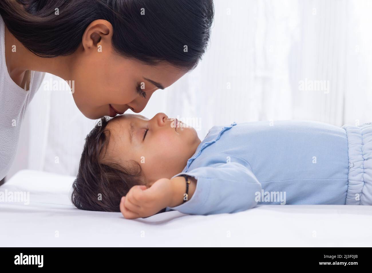 Portrait of mother kissing sleeping baby's forehead Stock Photo