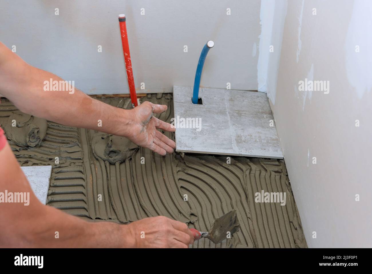 Man placing ceramic floor tile in position over adhesive Stock Photo