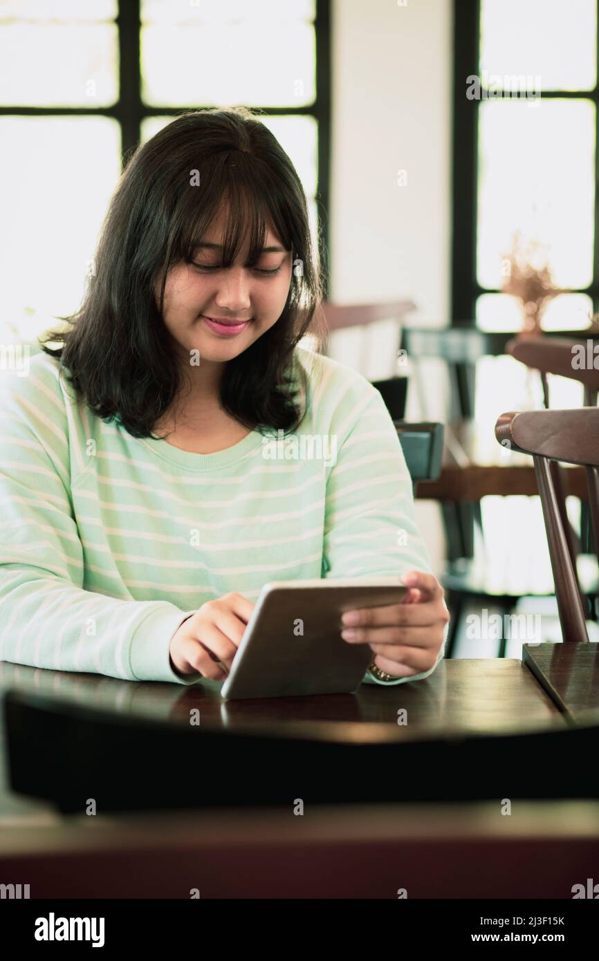 asian younger woman reading message on computer tablet with smiling face Stock Photo