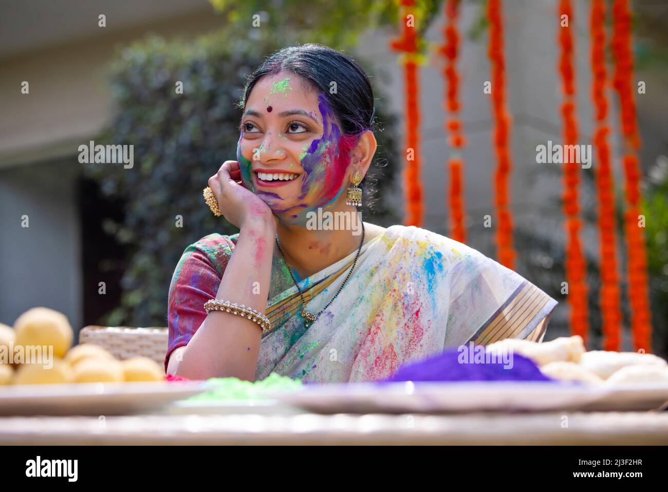 Portrait happy middle aged woman looking elsewhere with hand on cheek on Holi Stock Photo
