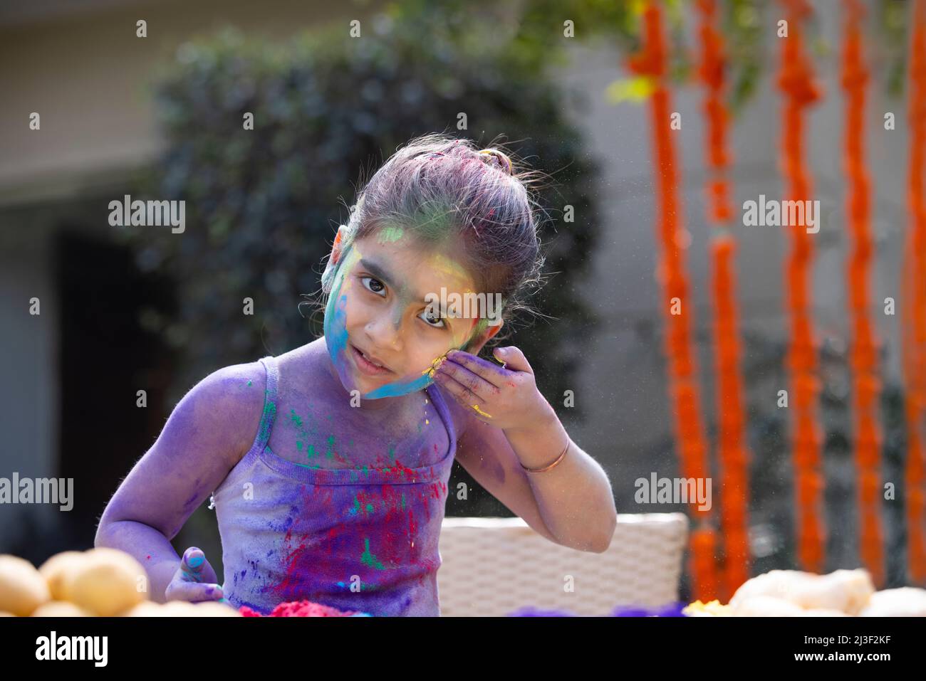 Little girl applying colour on her own face by herself on Holi Stock Photo