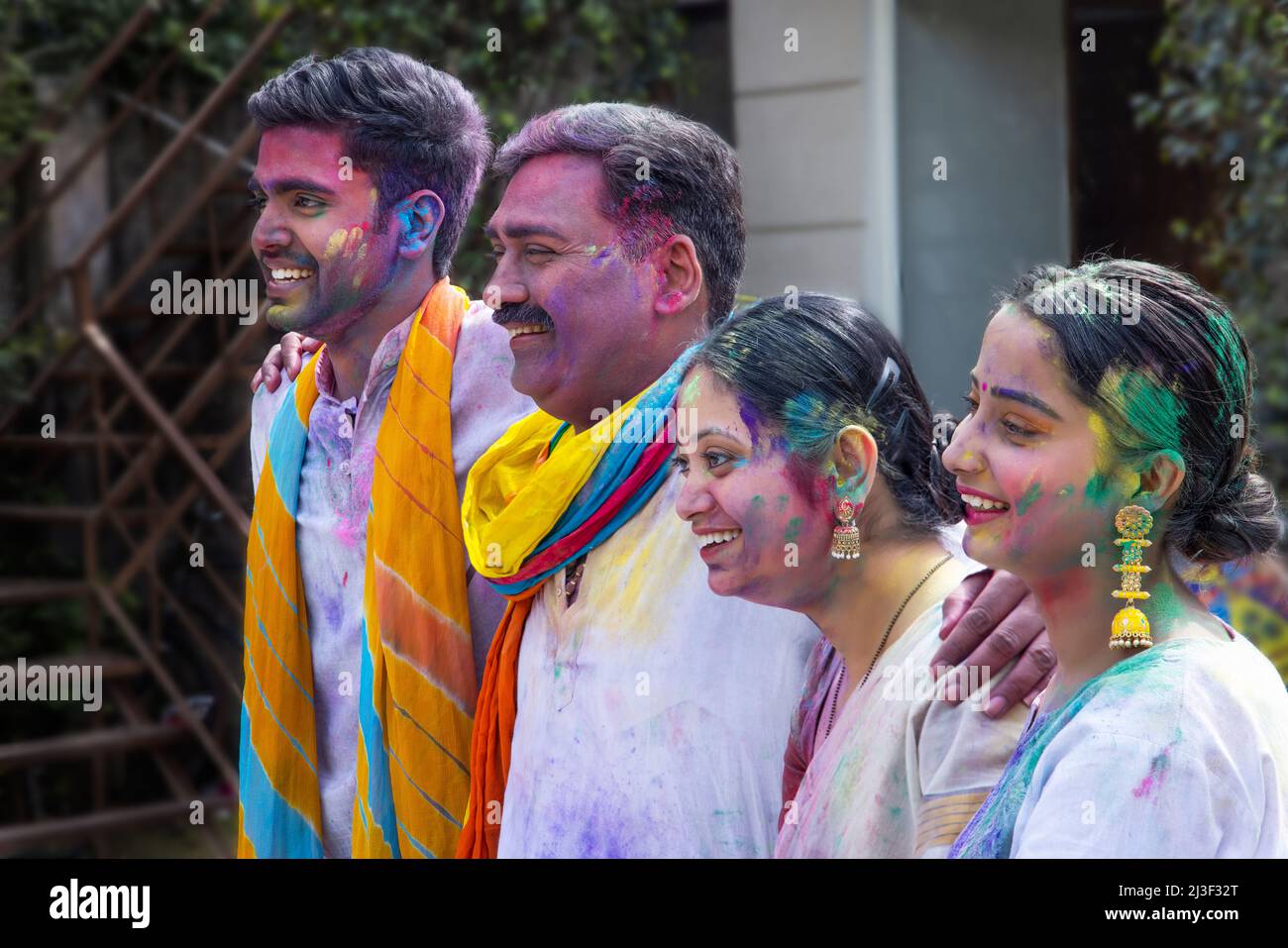 Happy family members standing in line with putting their hands on each other's shoulders and looking at the camera with smiling faces on Holi Stock Photo