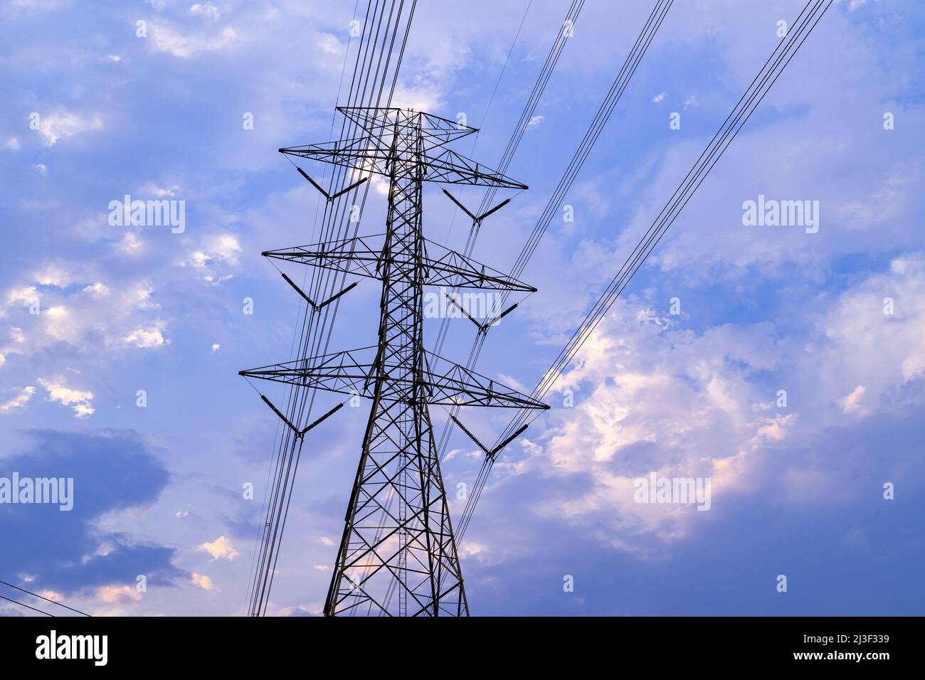 Evening clouds moving behind power line tower during sunset Stock Photo