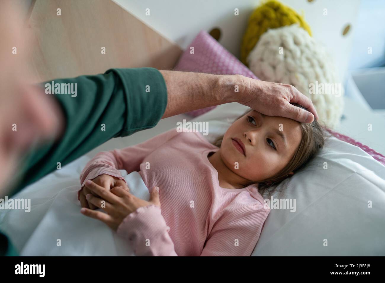 Grandfather taking care of his ill granddaughter lying in bed. Stock Photo