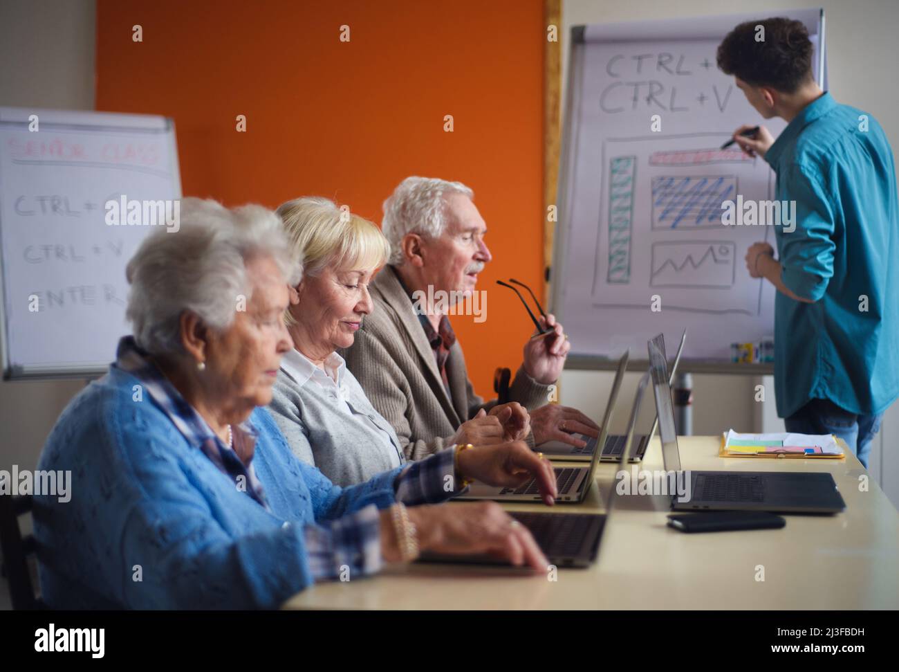 Senior group in retirement home with young instructor learning together in computer class Stock Photo