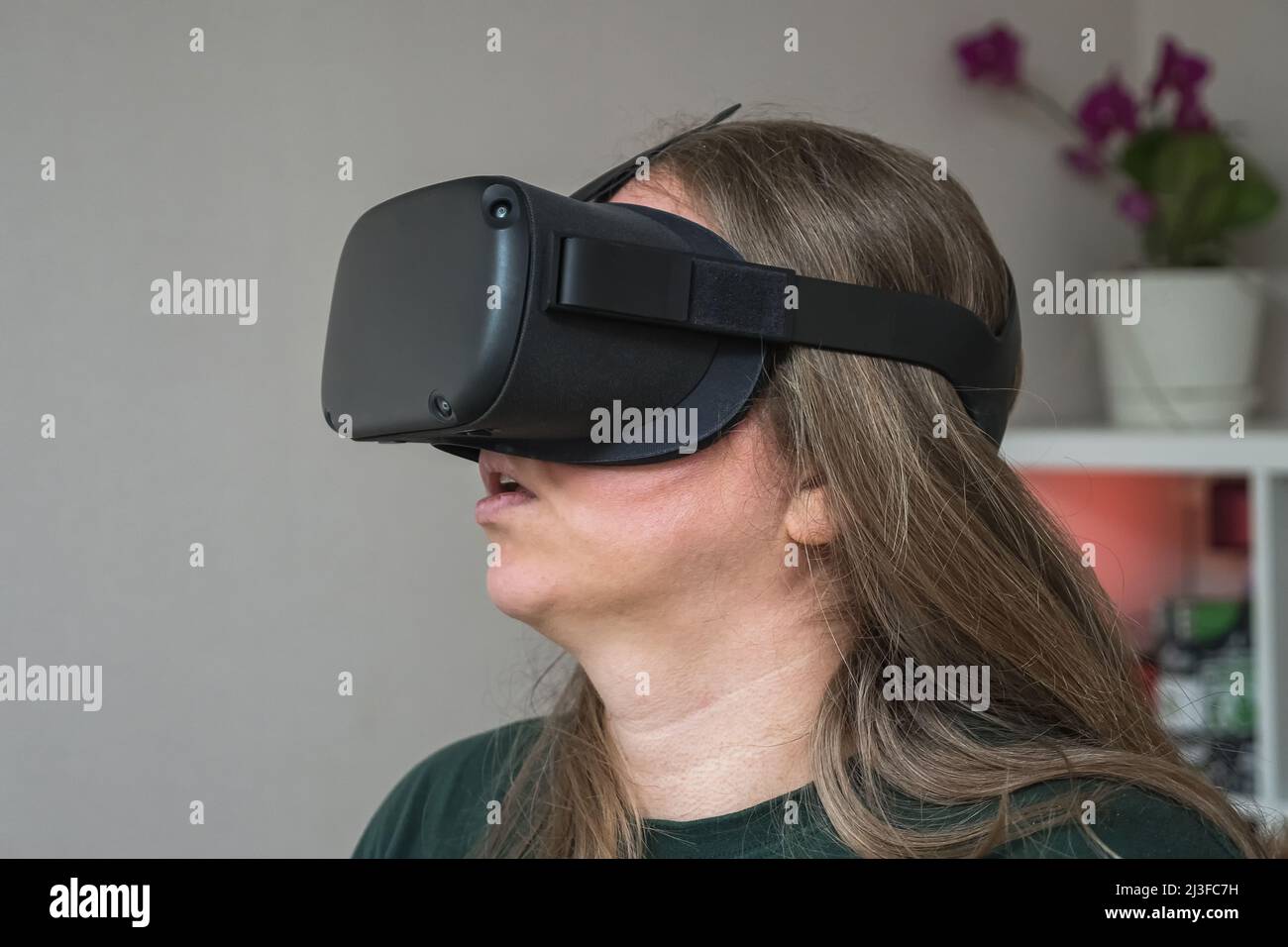 Close-up of a girl's head in a virtual reality helmet. A woman travels in the meta universe while standing in her room. VR glasses for gaming, educati Stock Photo