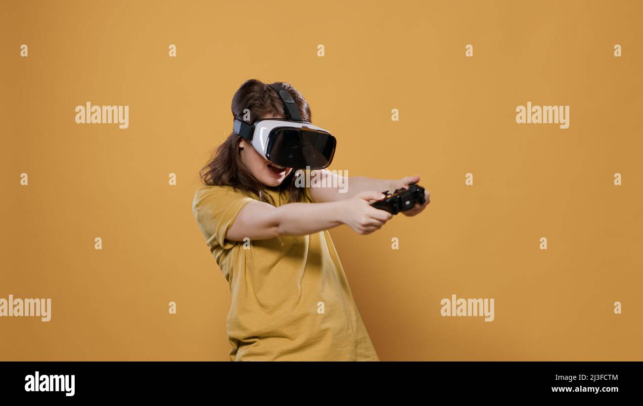 Woman playing game using vr goggles and console controller trying to win difficult level in studio. Gamer girl having intense experience with virtual reality looking at 3D surrounding enviroment. Stock Photo