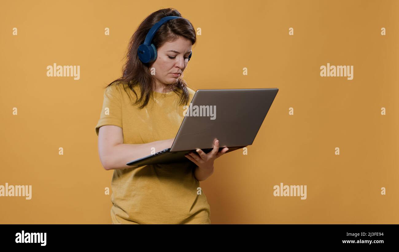 Casual woman wearing wireless headphones holding laptop and typing on ...