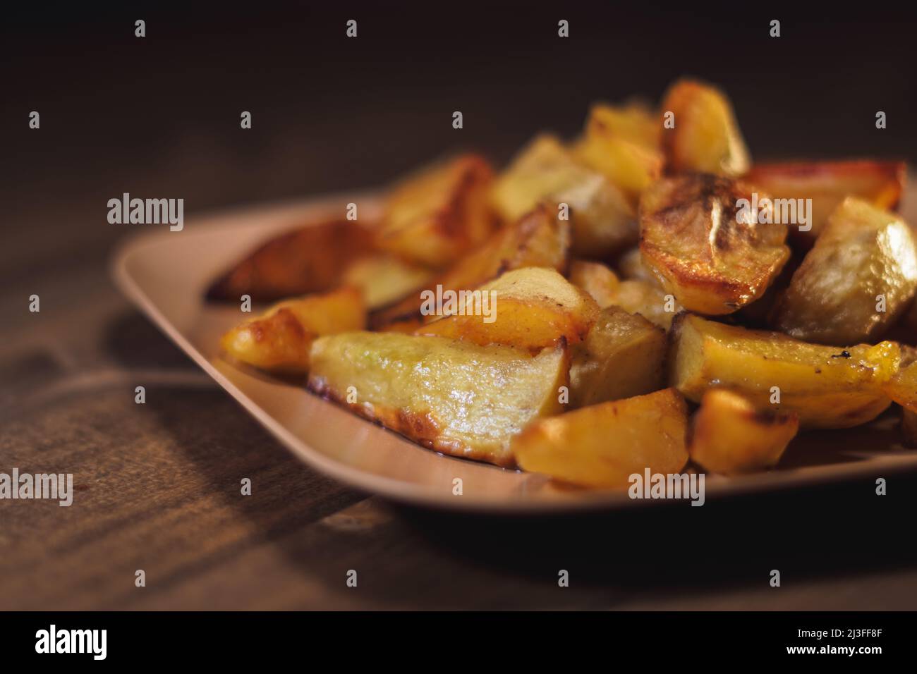 Baked crispy potatoes in a brown plate on a wooden table Stock Photo