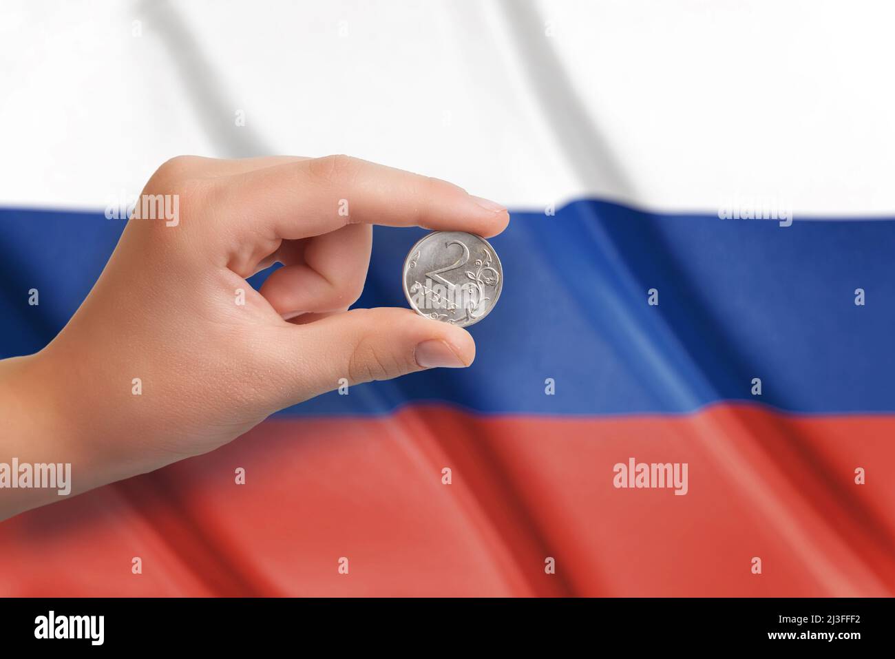 Russian ruble coin in hand. Fag of Russia in the background Stock Photo