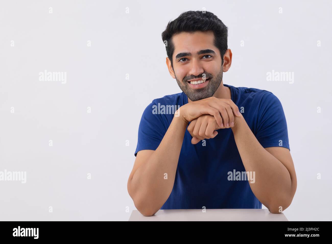 Studio shot of a happy young man looking at the camera with keeping hands under chin Stock Photo