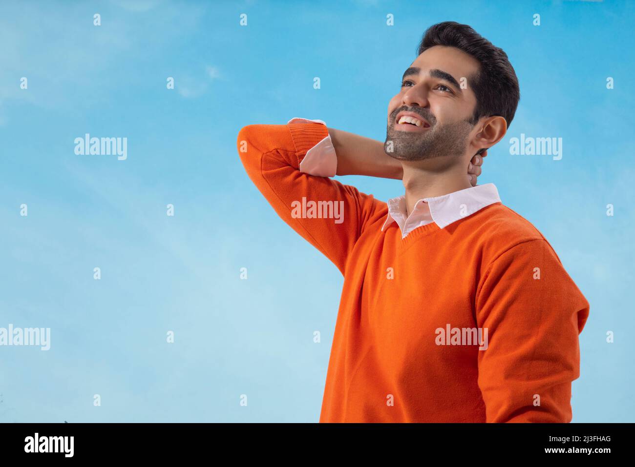 Happy man standing under the blue sky with his hand on neck Stock Photo