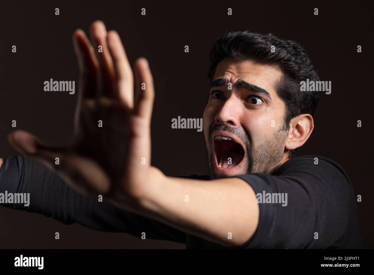 Portrait of a frightened young man looking away, raising hand and shouting Stock Photo