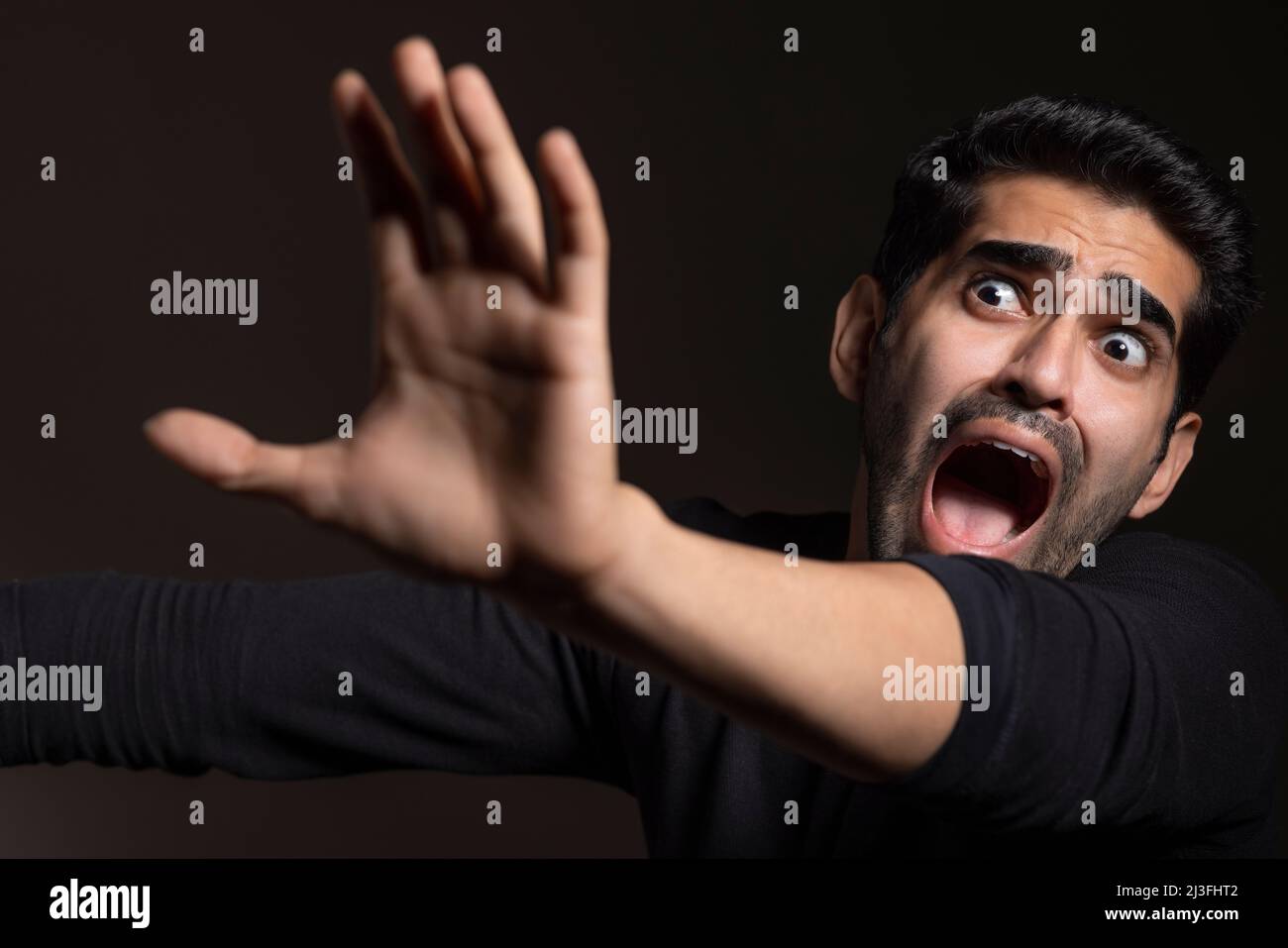 Portrait of a frightened young man looking away, raising hand and shouting Stock Photo