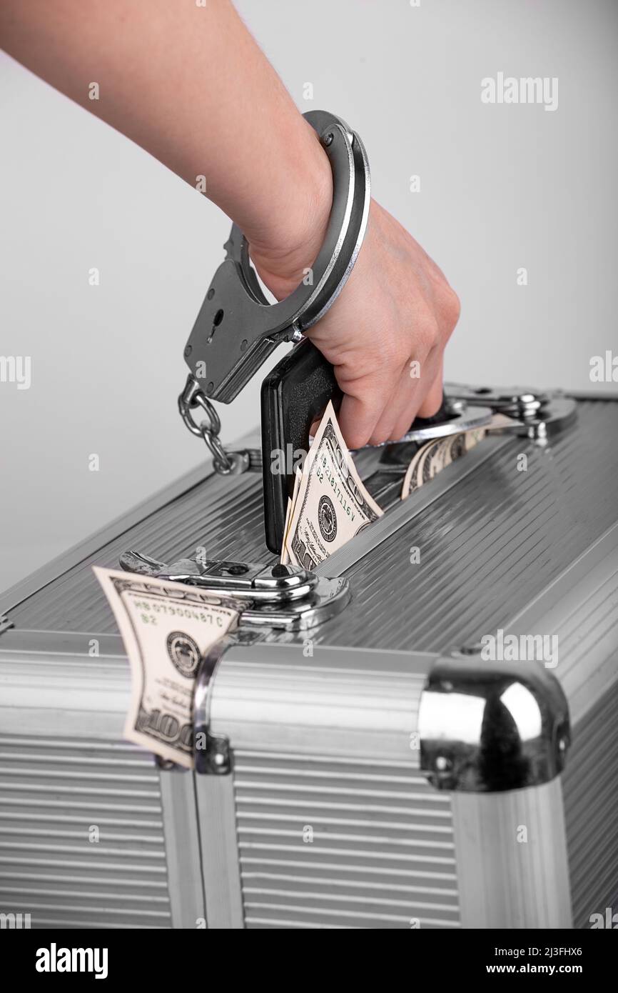 a man's hand handcuffed to a briefcase with dollars sticking out of it