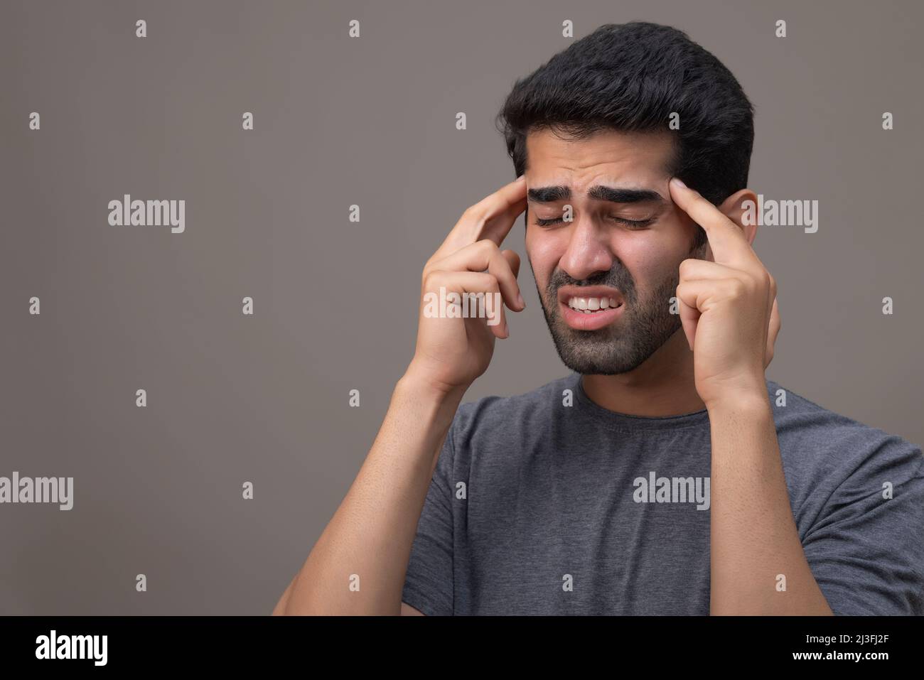 Portrait of a young man suffering from headache with hands on forehead Stock Photo