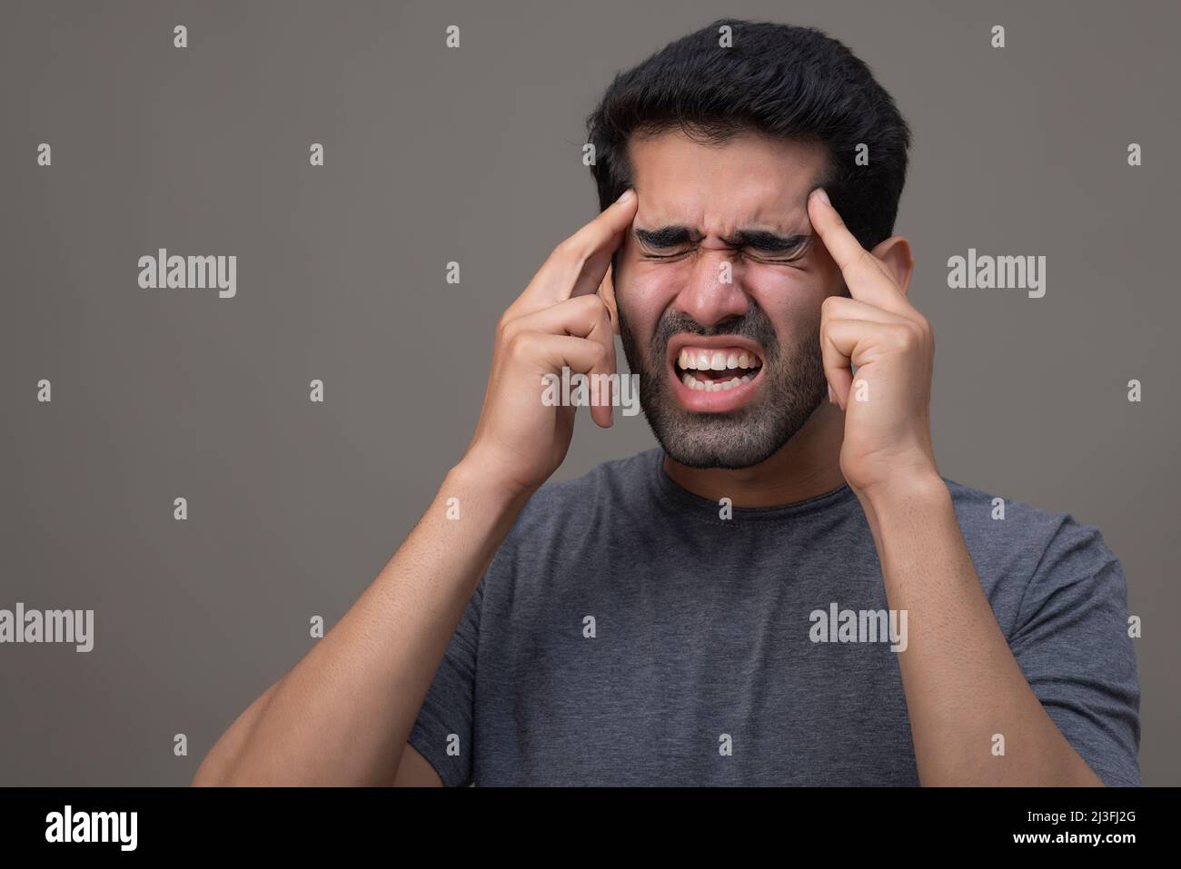 Portrait of a young man suffering from headache with hands on forehead Stock Photo