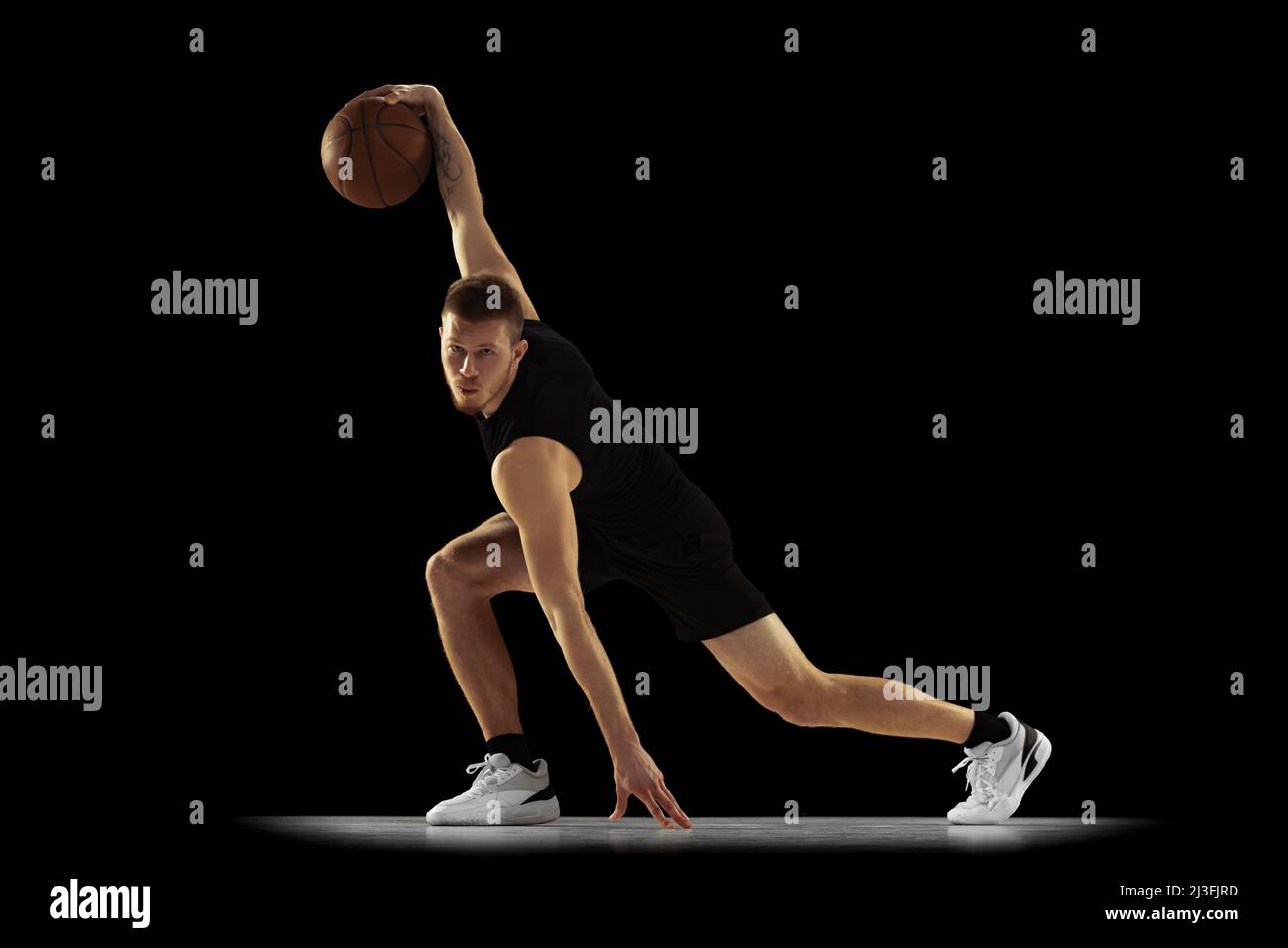 Ground move. Dynamic portrait of young man, basketball player in black