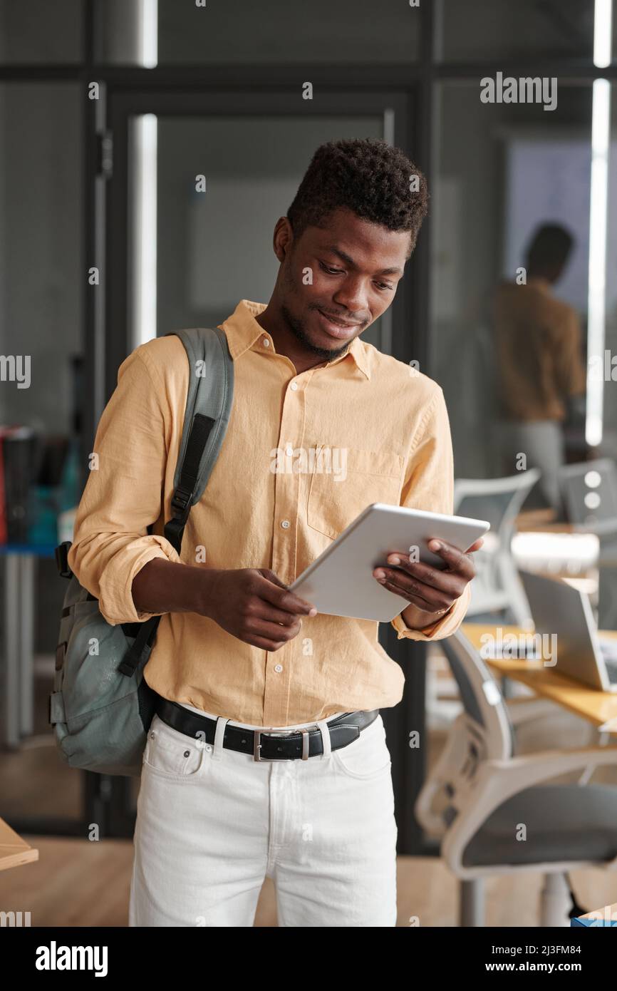 Smiling young Black guy with satchel checking information on tablet in coworking space Stock Photo