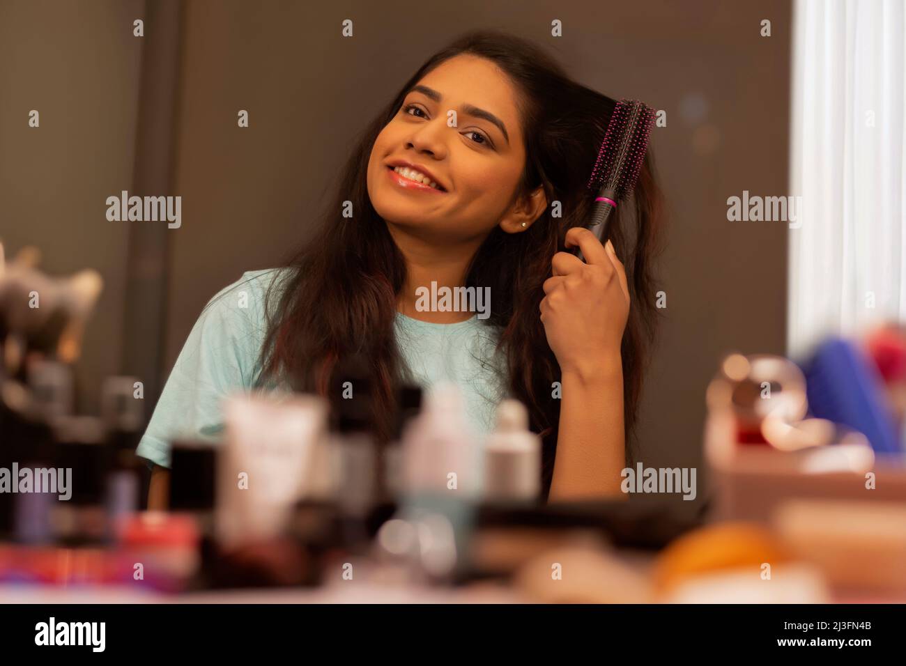 Young woman combing her hair in front of mirror Stock Photo