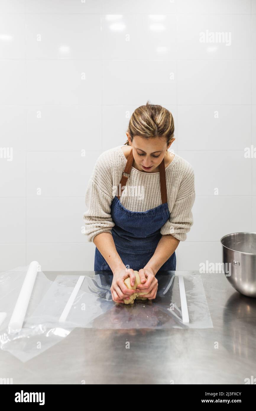 Female baker kneading dough on table in bakery Stock Photo