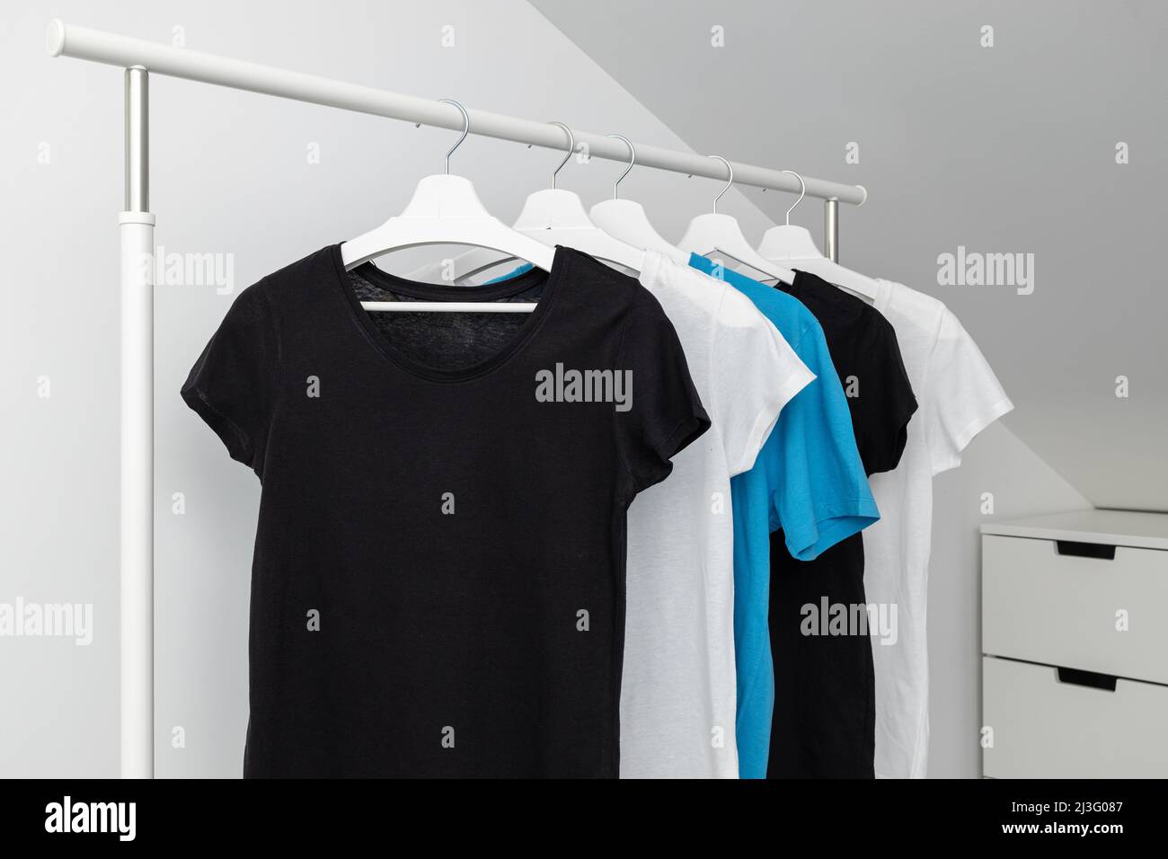 Group of Assorted t-shirts hanging on white hangers. Clothing rack. Template, mock up. Stock Photo