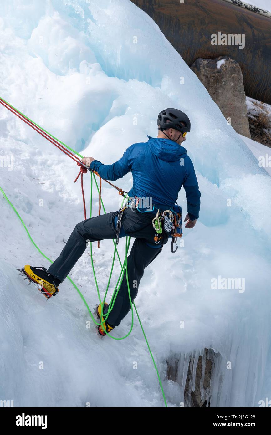 An ice climber belaying his climbing partner who is climbing up an ice