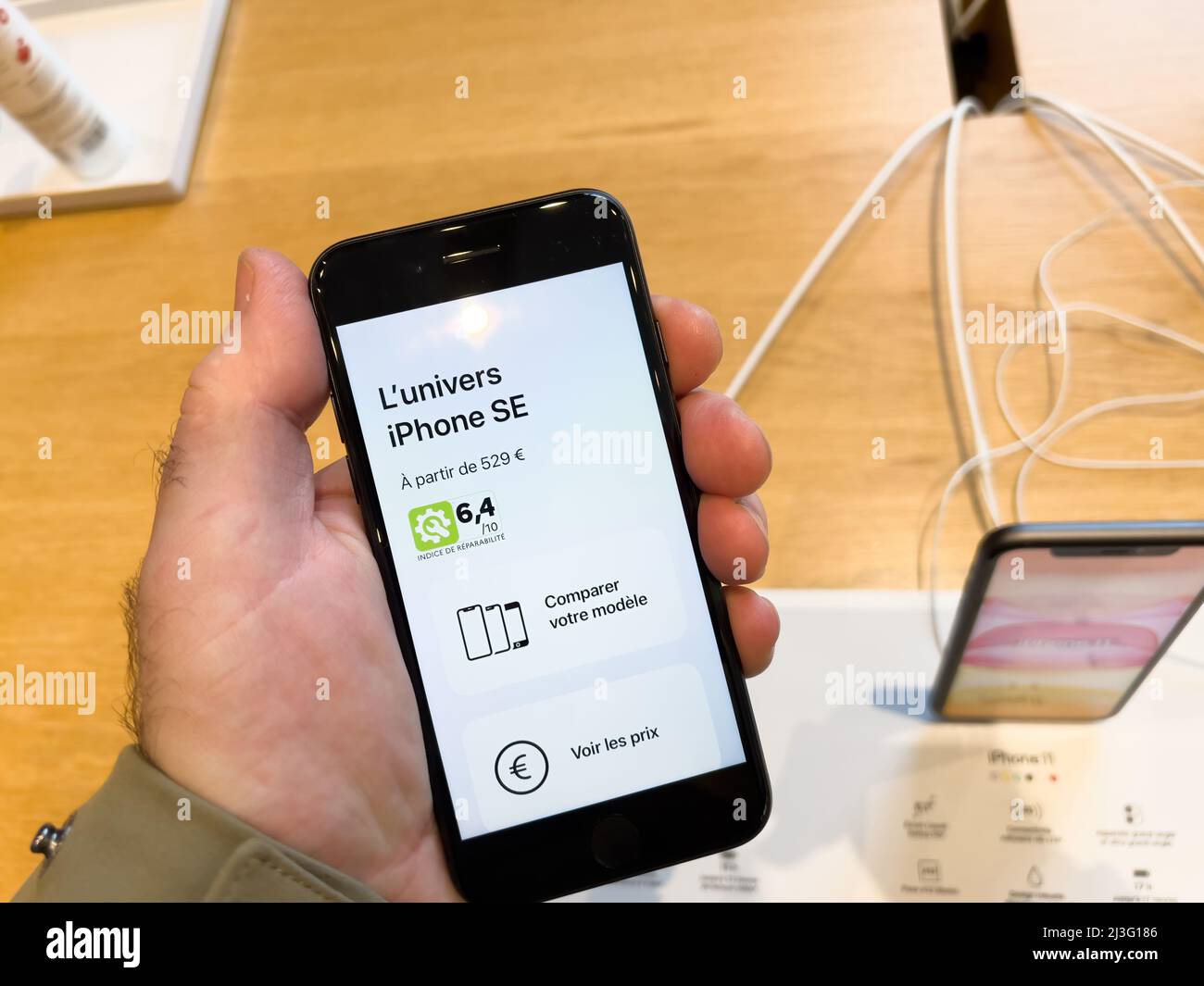 Paris, France - Ap 7, 2022: Male hand holding new latest Apple Computers iPhone SE smartphone with compare screen and repairability index Stock Photo