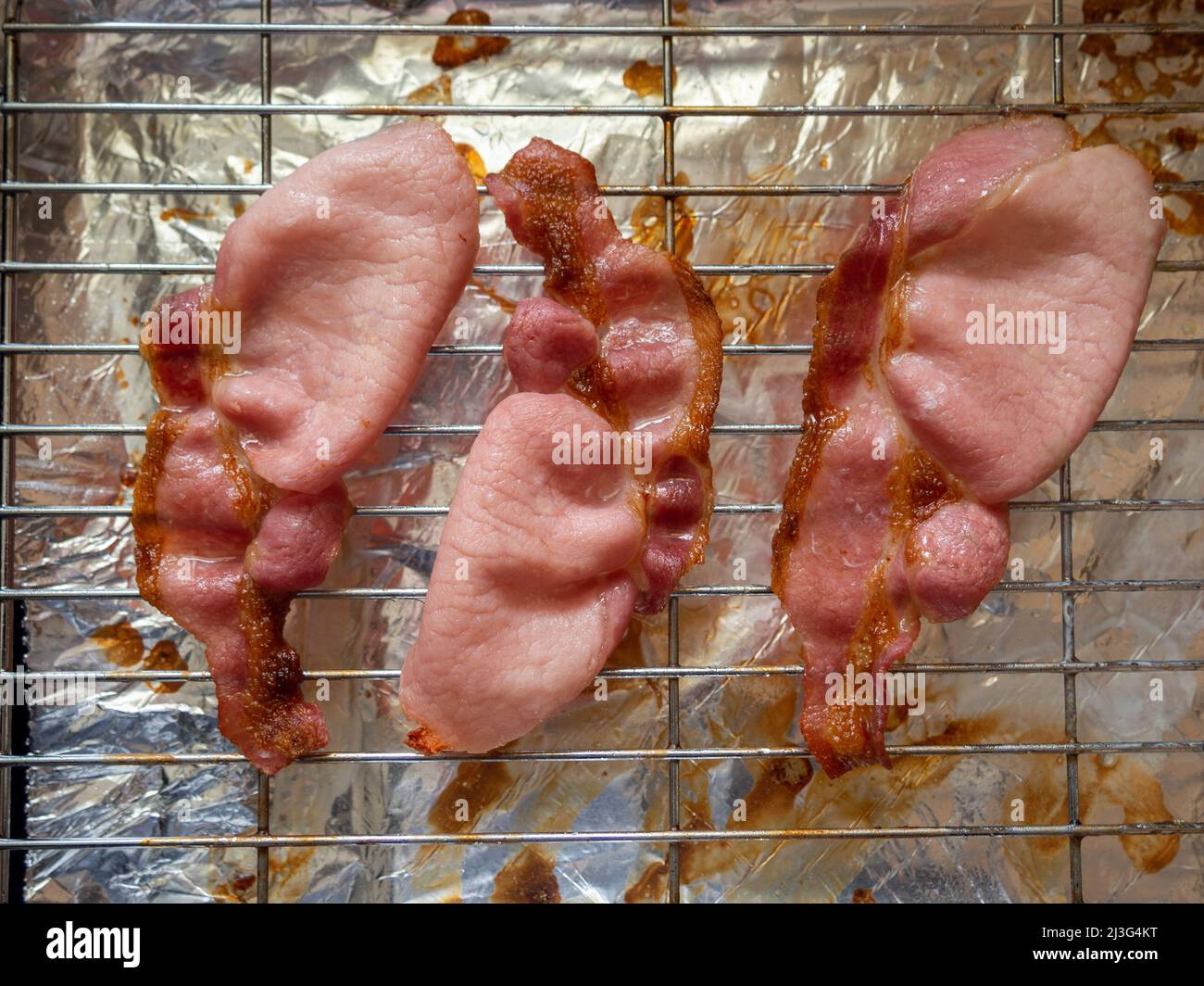 Three freshly grilled rashers of bacon on a domestic grill pan. Stock Photo